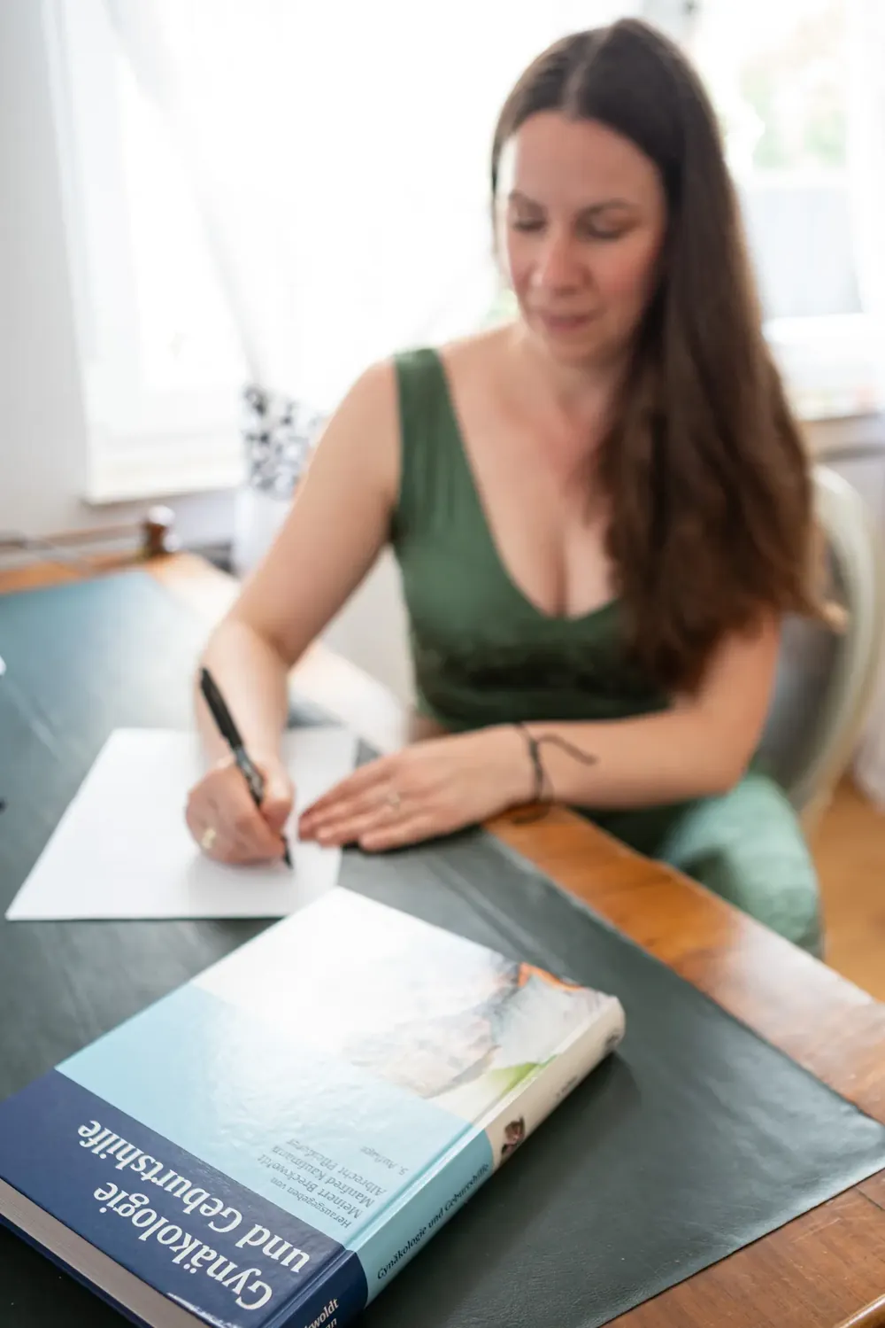Dr. Michaela Fischbach schreibt am Schreibtisch, davor ein Fachbuch zur Gynäkologie
